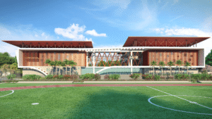 Modern two-story building with a red lattice facade and glass atrium, beside a running track and green field.