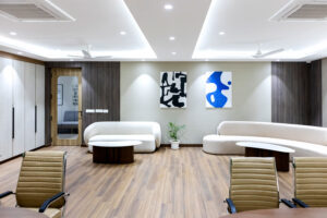 Modern office lounge with curved white sofas, round coffee tables, and abstract black and blue wall art.