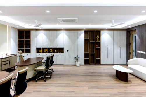 Modern office conference area with a curved wooden desk, beige ergonomic chairs, and tall light-gray storage cabinets along the back wall.